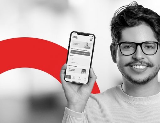 capa do artigo sobre do App DOK Despachante | Descrição: homem jovem branco, com barba e bigode, usa óculos e segura um celular ao lado do rosto olhando para a câmera; a foto está em preto e branco.